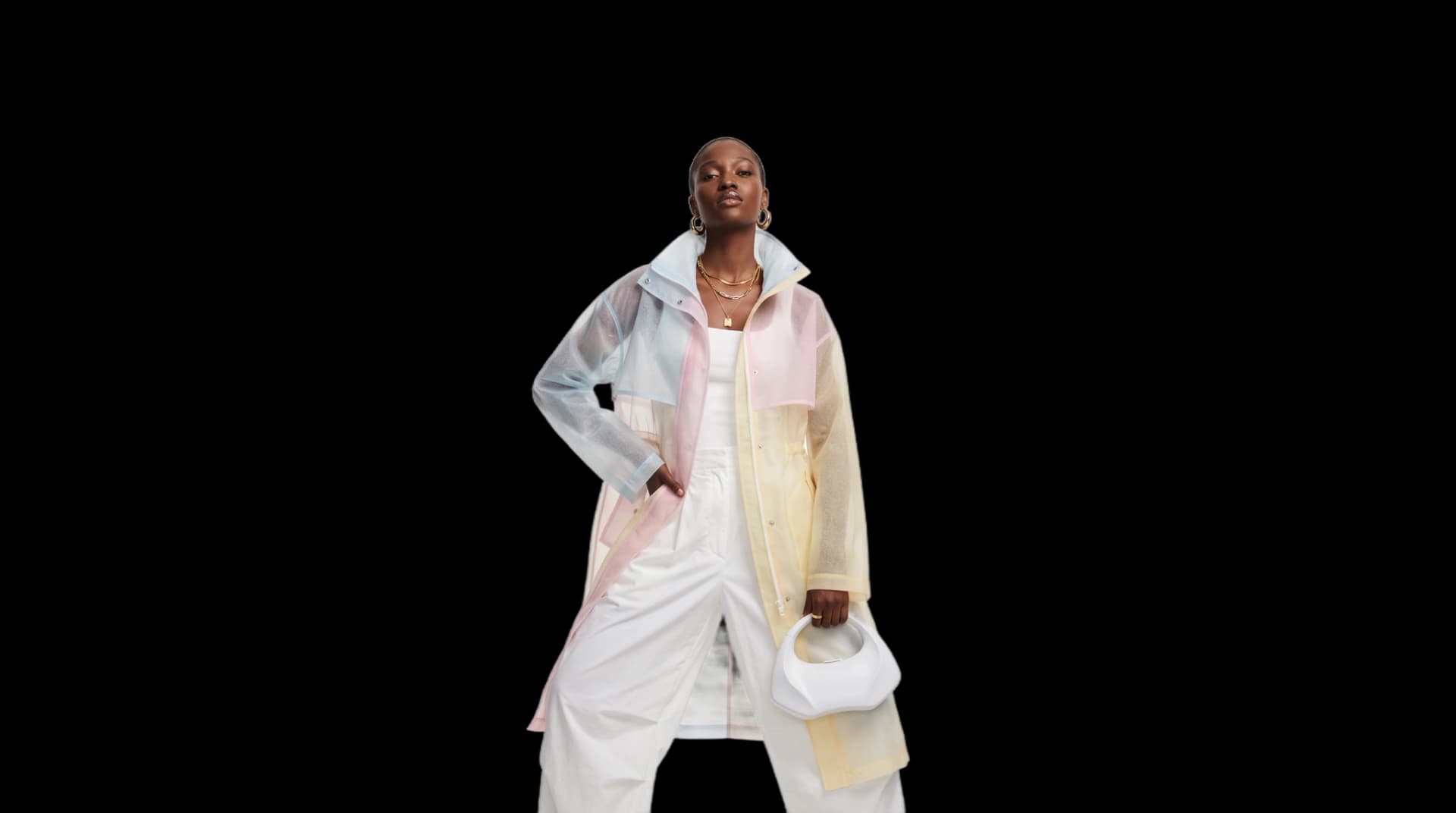 A model in a translucent colour-block raincoat in pale blue, pink and yellow over white trousers, holding a small white bag, cut out on a plain ground