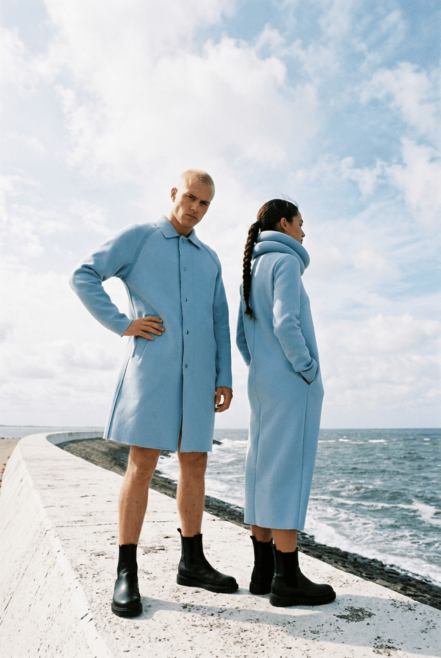 Two models in powder-blue coats on a white sea dike