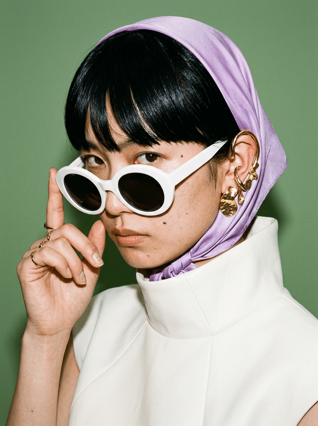 Close-up of a female model in white oval sunglasses on a sage-green backdrop