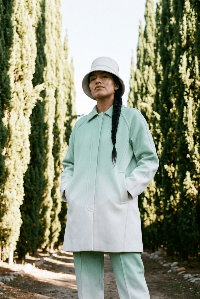 Female model in a mint coat with a long braid in a cypress alley