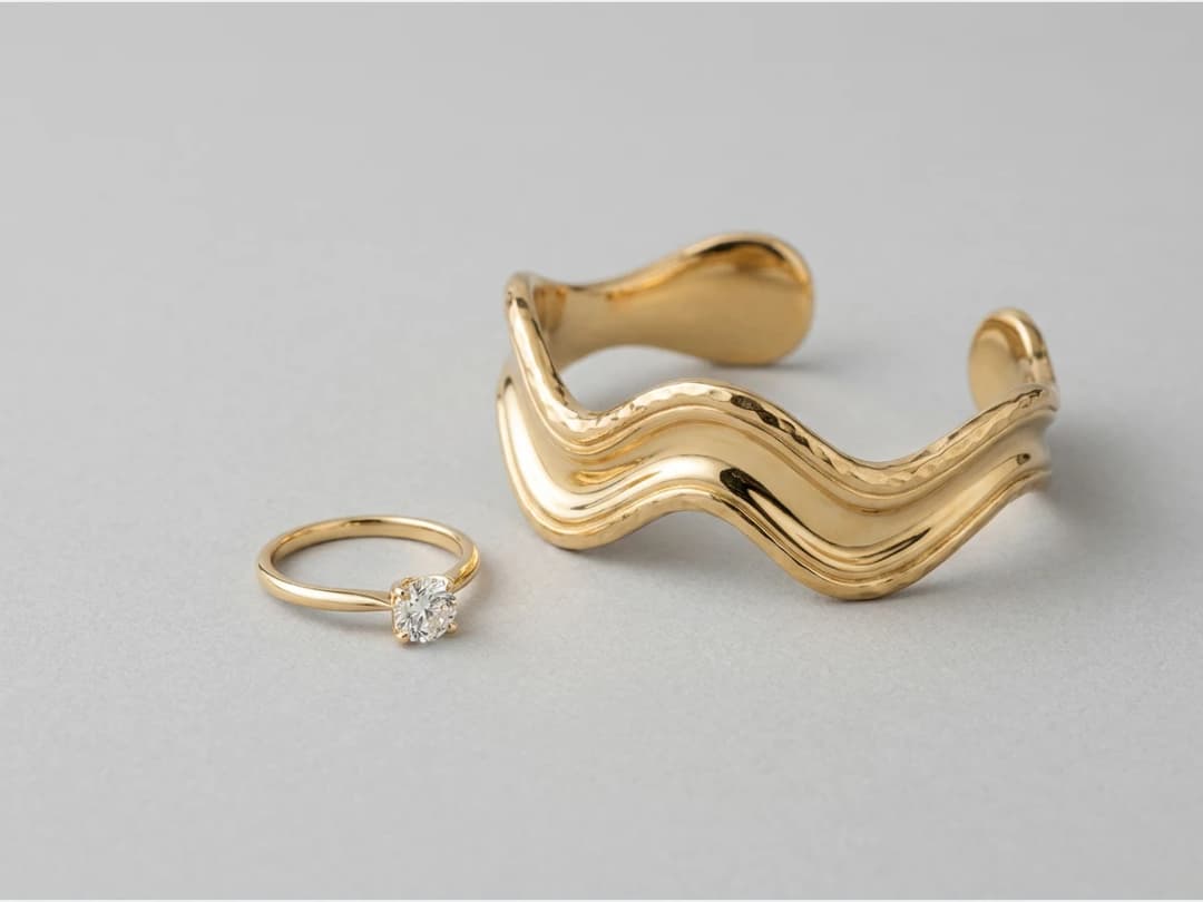 a fine gold ring set with a single stone, product shot, a second design, a sculptural gold cuff bracelet