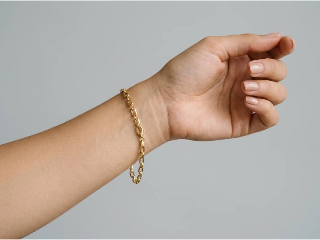 a close shot of a wrist wearing a bracelet, a gold chain bracelet