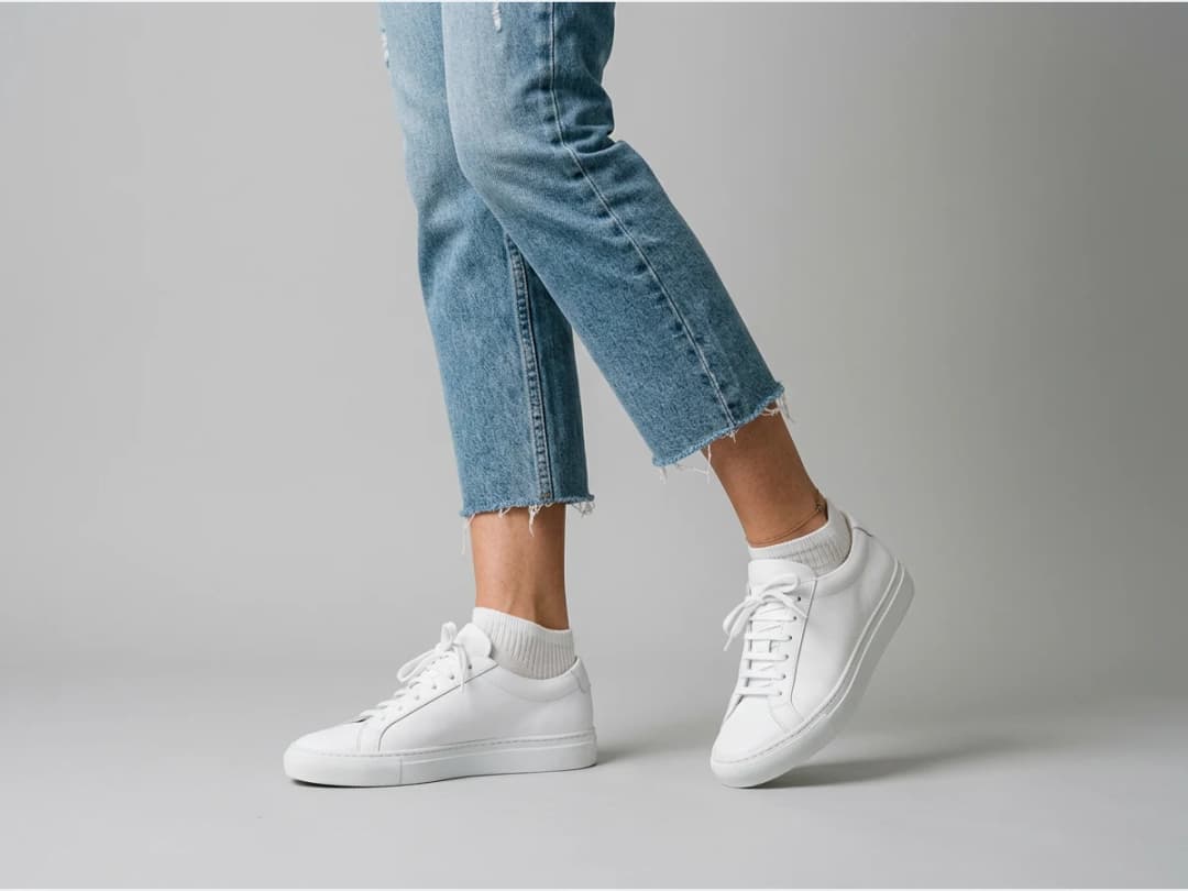 a model's legs and feet wearing designer shoes, white sneakers with cropped jeans