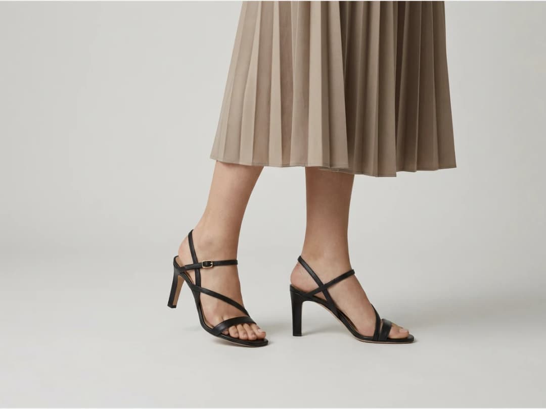 a model's legs and feet wearing designer shoes, heeled sandals with a midi skirt